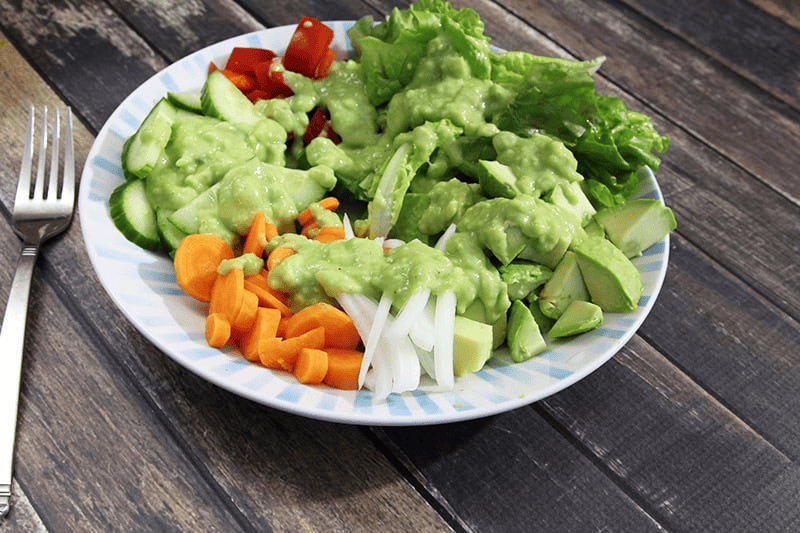 A colourful salad featuring fresh lettuce, avocado, cucumbers, tomatoes, carrots, and onions, all topped with creamy avocado dressing, served on a striped plate. This vibrant presentation highlights the knife's ability to achieve clean, precise cuts on fresh produce, as emphasized in the review.